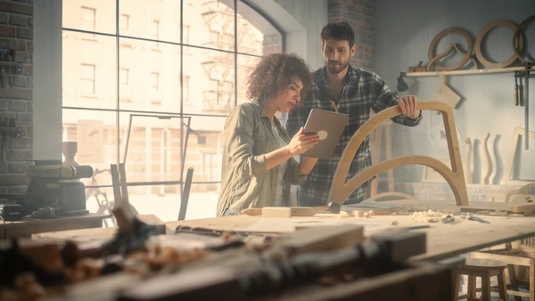Atelier d'artisanat intérieur avec deux artisans travaillant ensemble sur une pièce de mobilier en bois courbé