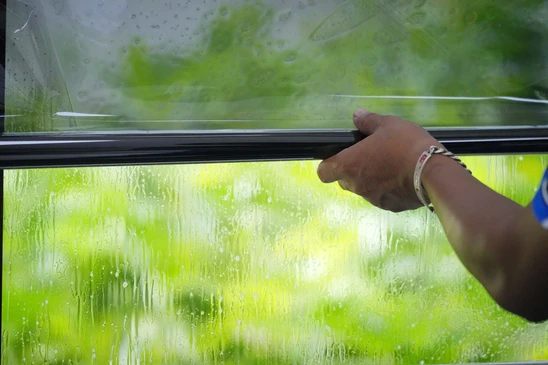 Un artisan professionnel en tenue de travail appliquant un film de protection transparent ou teinté sur une baie vitrée ou une fenêtre d'intérieur, utilisant une raclette pour lisser le film et éliminer les bulles d'air, dans un environnement résidentiel moderne.